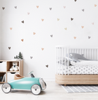 Soft neutral-tone heart decals scattered on a nursery wall above a wooden toy shelf and teddy bear